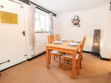 A dining room with a wooden table set for four near a window with patterned curtains at Phloxhaven in Reedham