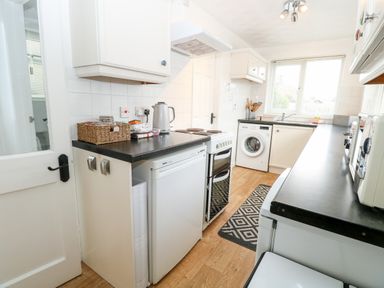 A kitchen with white cabinets black countertops a washing machine a refrigerator a stove and a window at Phloxhaven in Reedham