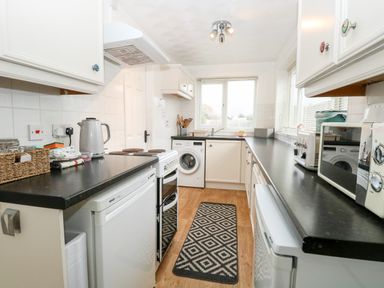 A kitchen with white cabinets black countertops a stove washing machine toaster microwave and patterned rug at Phloxhaven in Reedham