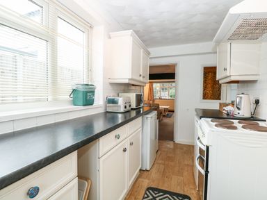 A kitchen with white cabinets black countertops a toaster microwave kettle and a white stove at Phloxhaven in Reedham