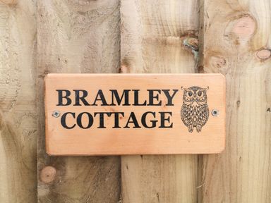 A wooden sign with an owl illustration and the text Bramley Cottage on a wooden background at Bramley Cottage in Henley near Langport