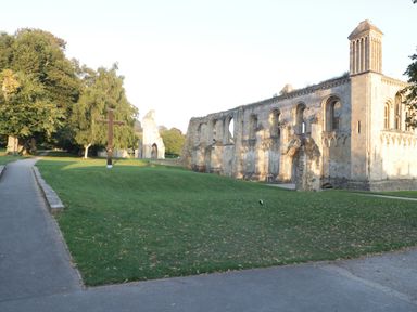 A stone church ruin with arched windows beside a grassy area with a wooden cross and walking paths in a park