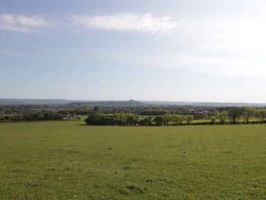 A wide grassy field with trees and a distant town under a partly cloudy sky at Bramley Cottage in Henley near Langport