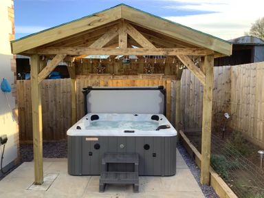An outdoor hot tub under a wooden gazebo with string lights and wooden fencing at Bramley Cottage in Henley near Langport