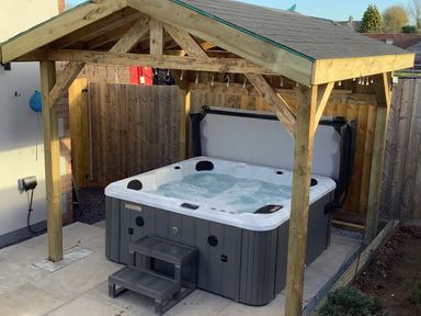 A hot tub with water and steps under a wooden pergola on a tiled patio