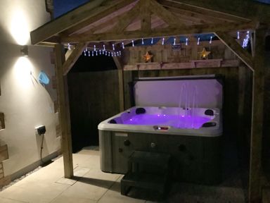 An outdoor hot tub with purple lights under a wooden gazebo with string lights and star decorations at Bramley Cottage Henley near Langport