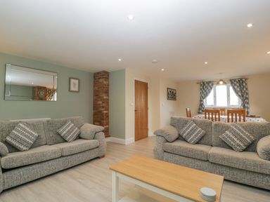 A living room area with two grey sofas and a wooden coffee table next to a dining table with wooden chairs and window at Bramley Cottage Henley near Langport