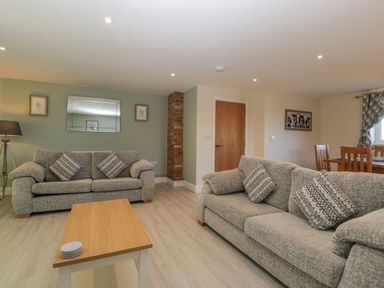 A living room with two gray sofas a wooden coffee table a tripod floor lamp a green feature wall with framed pictures and a mirror at Bramley Cottage Henley near Langport