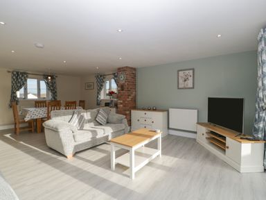 A living room with a sofa a coffee table a dining table a television and a sideboard at Bramley Cottage in Henley near Langport