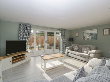 A living room with sofas a coffee table a television and glass doors at Bramley Cottage in Henley near Langport