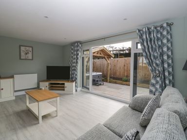 A living room with a sofa coffee table television and large glass doors opening to a patio at Bramley Cottage in Henley near Langport