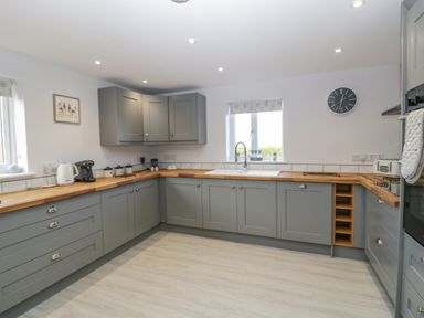 A kitchen with grey cabinets wooden countertops a sink under a window and appliances at Bramley Cottage in Henley near Langport