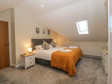 A bedroom with a bed covered with white and orange bedding a nightstand with lamp a skylight and a chest of drawers at Bramley Cottage Henley near Langport