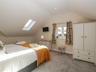 A bedroom with a double bed an orange blanket a chest of drawers a wardrobe a window with curtains and a skylight at Bramley Cottage in Henley near Langport