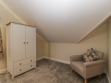 A small room with a white wardrobe and an armchair with pillows under a sloped ceiling at Bramley Cottage in Henley near Langport