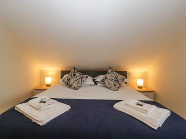 A bedroom with a bed with folded towels on a navy blanket and bedside tables with lamps at Bramley Cottage Henley near Langport