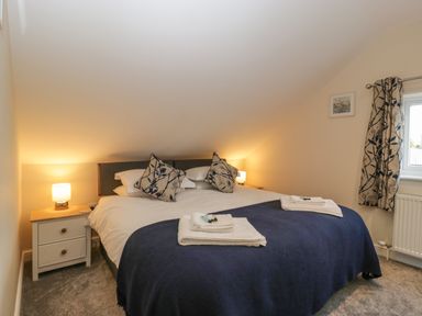 A bedroom with a large bed two bedside tables lamps and a window with patterned curtains at Bramley Cottage in Henley near Langport