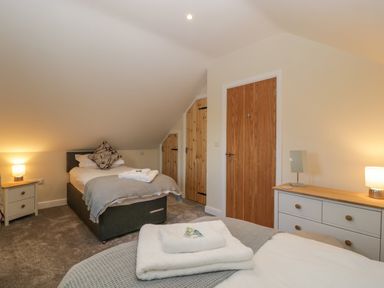 A bedroom with two single beds bedside table dresser and wooden doors at Bramley Cottage in Henley near Langport