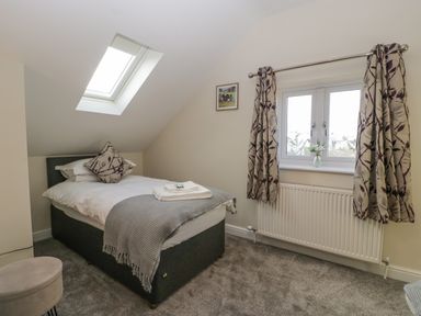 A bedroom with a single bed under a skylight window and a double window with curtains at Bramley Cottage in Henley near Langport