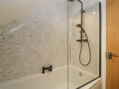 A bathroom with a bathtub with black faucet shower with glass screen and wooden door at Bramley Cottage in Henley near Langport