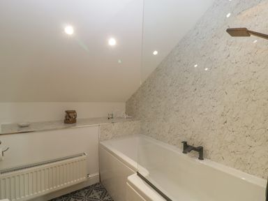 A bathroom with a bathtub shower radiator and shelf with toiletries at Bramley Cottage Henley near Langport