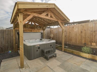 A wooden gazebo with a hot tub and steps on a stone patio in a fenced garden at Bramley Cottage in Henley near Langport