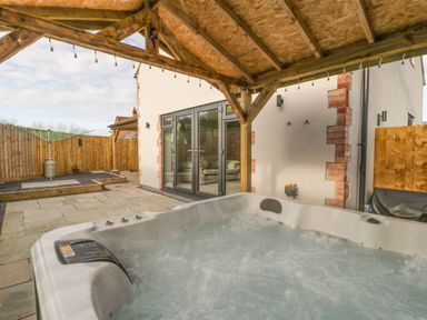 A bubbling hot tub under a wooden pergola in a backyard with patio doors at Bramley Cottage in Henley near Langport