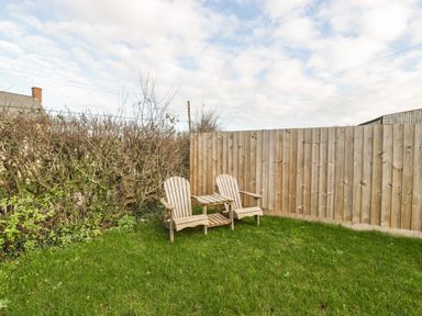 Two wooden chairs with an attached table on grass next to a wooden fence and bushes at Bramley Cottage in Henley near Langport