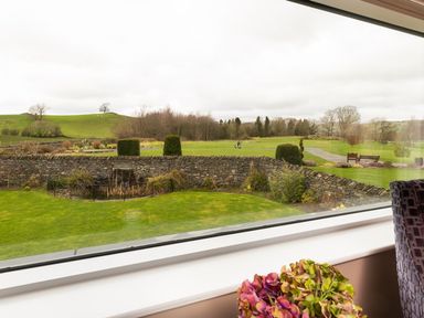 A view of a garden with a stone wall and greenery outside a window at Carus House at Carus Green Golf Club in Kendal