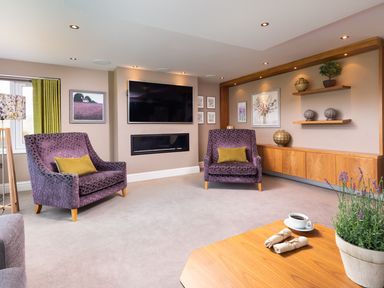 A living room with two purple armchairs facing a wall-mounted TV and a modern fireplace at Carus House at Carus Green Golf Club in Kendal