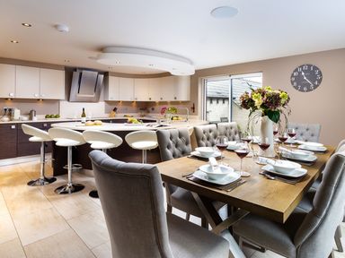 A kitchen and dining area with a wooden dining table set for eight and a kitchen island with white bar stools at Carus House at Carus Green Golf Club in Kendal