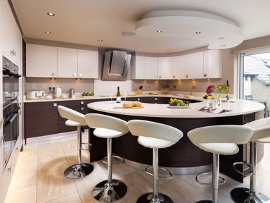 A modern kitchen with a curved island and white stools at Carus House at Carus Green Golf Club in Kendal