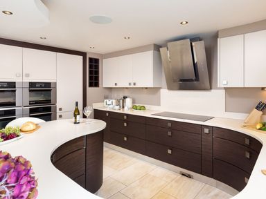 A modern kitchen with curved countertops dark lower cabinets white upper cabinets built in ovens and a wine bottle with glass on the counter at Carus House at Carus Green Golf Club Kendal