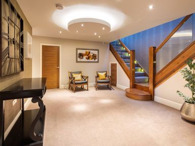 A hallway with two chairs and a table near a wooden staircase at Carus House at Carus Green Golf Club in Kendal