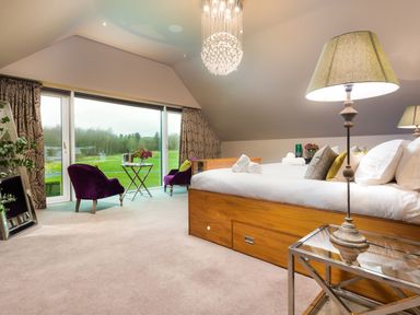A bedroom with a wooden bed white linens two purple chairs and a large window showing a view of greenery at Carus House at Carus Green Golf Club in Kendal