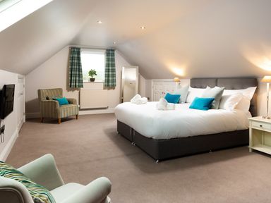 A bedroom with a large bed chairs a window with curtains and a mounted television at Carus House at Carus Green Golf Club in Kendal