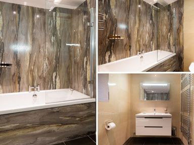 A bathroom with a bathtub featuring a glass panel shower screen and stone wall cladding and a washbasin with mirror and towel radiator at Carus House at Carus Green Golf Club Kendal