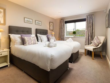 A bedroom with two single beds side by side a chair by the window and bedside tables at Carus House at Carus Green Golf Club Kendal