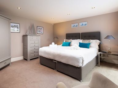 A bedroom with a double bed pillows and towels bedside tables with lamps a chest of drawers an armchair and framed pictures on the walls at Carus House at Carus Green Golf Club Kendal