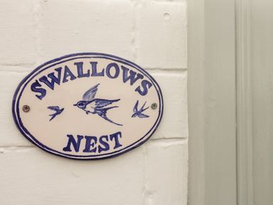 An oval sign with illustrations of swallows and the text Swallows Nest on a white painted brick wall at Swallows Nest in Whitby