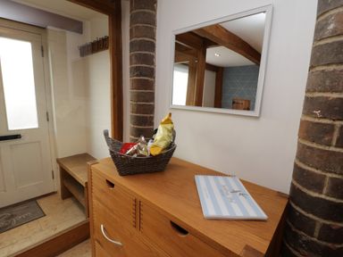A hallway with a wooden cabinet holding a basket of snacks and a book beside a brick pillar and a mirror at Swallows Nest Whitby