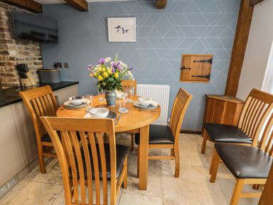 A dining table with six chairs and a flower vase set for four people in a kitchen at Swallows Nest in Whitby