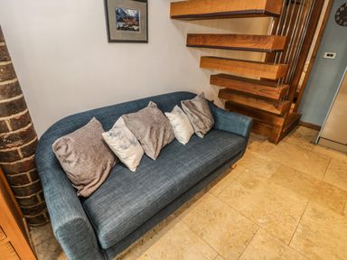 A blue sofa with five pillows near wooden stairs and a brick pillar
