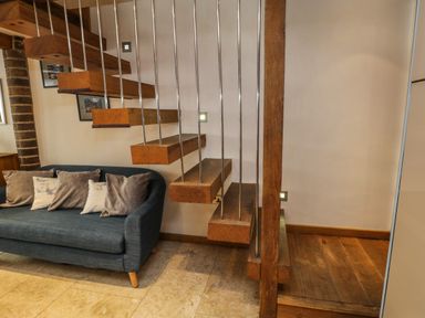 A living area with a blue sofa and wooden floating stairs with metal railings at Swallows Nest in Whitby