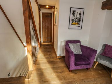 A hallway with wooden floor and beams with a purple armchair and a grey armchair with cushions at Swallows Nest Whitby