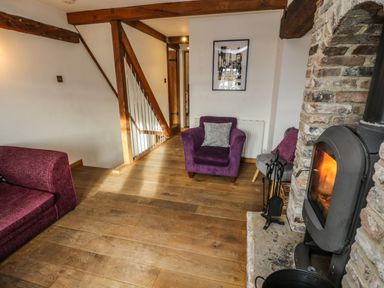 A living room with a wood burning stove wooden floor and purple armchairs at Swallows Nest in Whitby