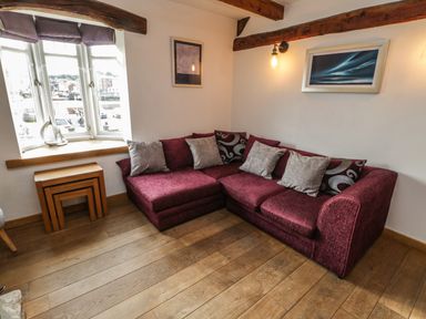 A corner with a maroon sectional sofa with cushions wooden nesting tables and a window with decorations at Swallows Nest in Whitby