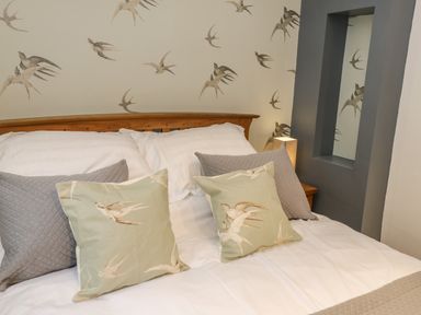A bed with white sheets and cushions with bird patterns in a room with bird wallpaper at Swallows Nest in Whitby