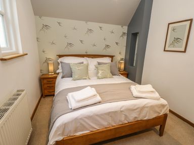 A bedroom with a wooden bed and bird patterned pillows and wallpaper at Swallows Nest in Whitby