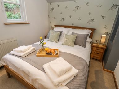 A bedroom with a wooden bed covered in white and grey bedding with folded towels on the bed a tray with croissants orange juice and a vase with yellow flowers at Swallows Nest in Whitby